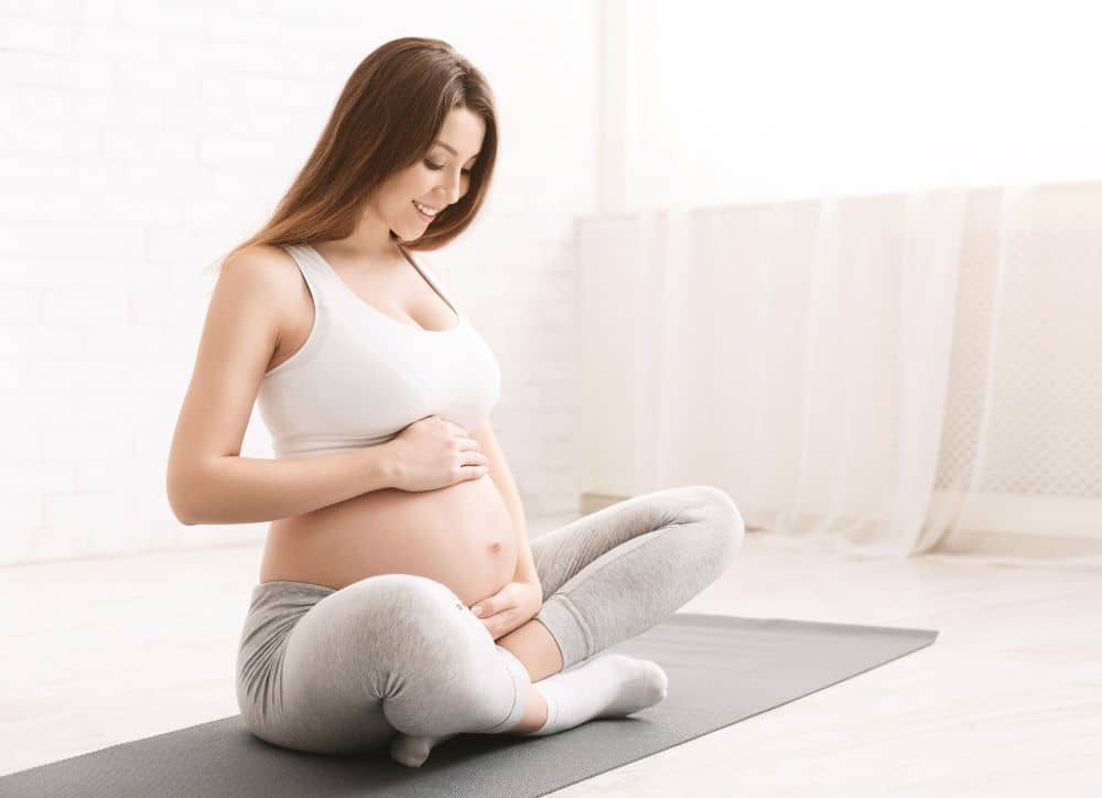Pregnant woman sitting on yoga mat after exercise.